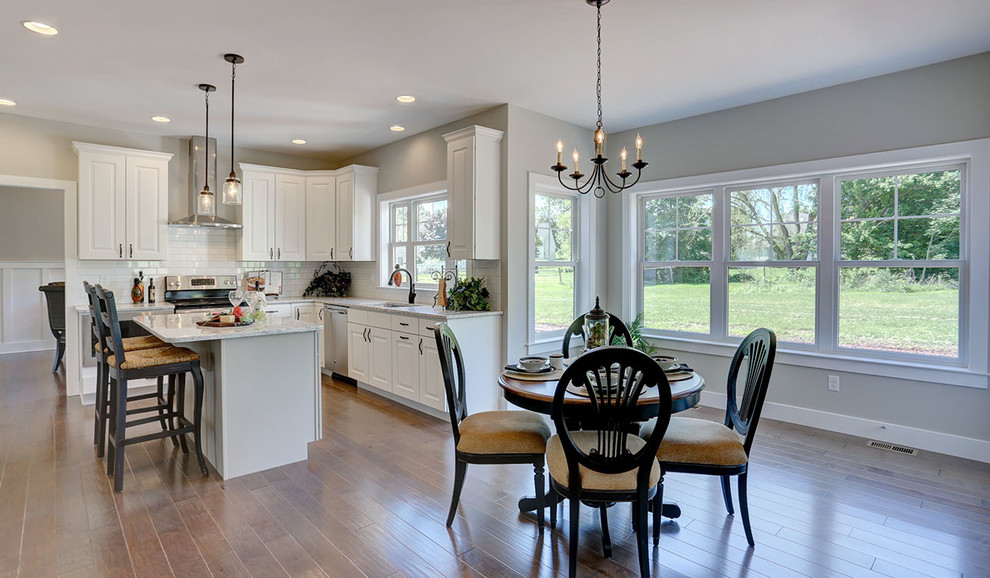 Example of a mid-sized country l-shaped medium tone wood floor eat-in kitchen design in Other with a double-bowl sink, white cabinets, quartz countertops, white backsplash, subway tile backsplash, stainless steel appliances, an island and beige countertops
