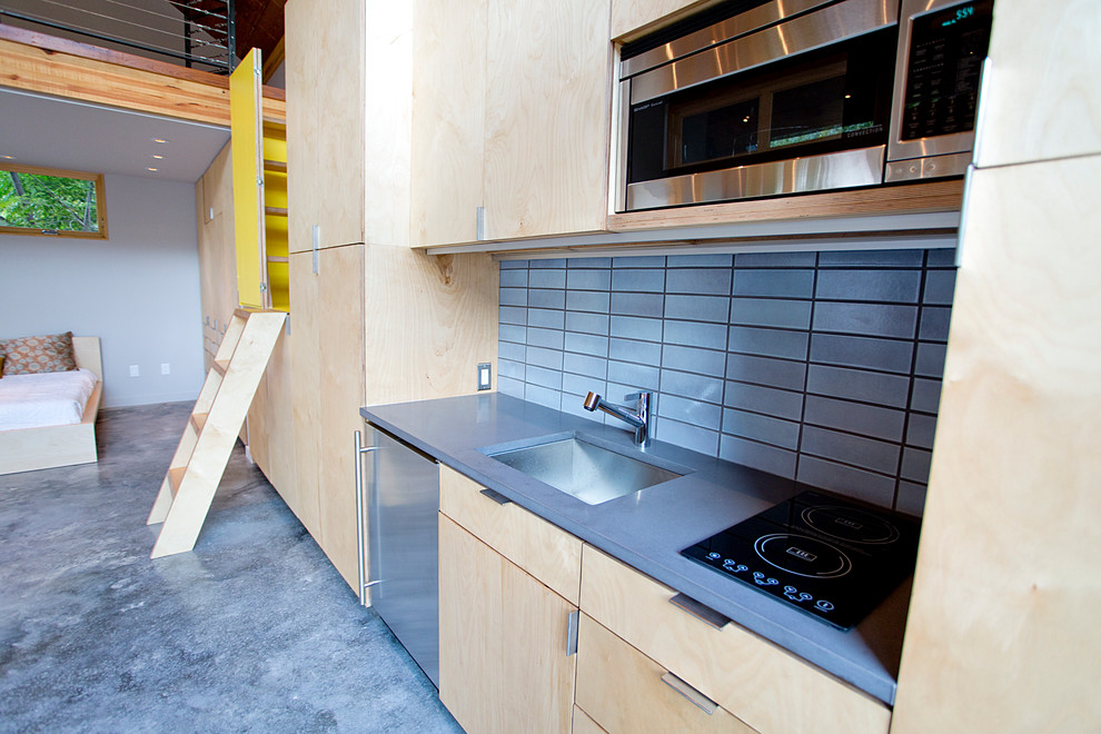 Foto på ett funkis linjärt kök, med en undermonterad diskho, släta luckor, skåp i ljust trä, granitbänkskiva, blått stänkskydd, stänkskydd i keramik, rostfria vitvaror och betonggolv