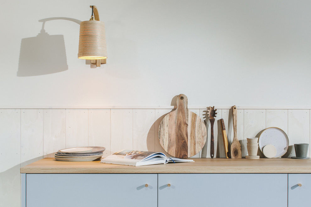 Foto på ett litet nordiskt brun linjärt kök med öppen planlösning, med en enkel diskho, släta luckor, grå skåp, träbänkskiva, vitt stänkskydd, stänkskydd i trä, integrerade vitvaror, målat trägolv och svart golv