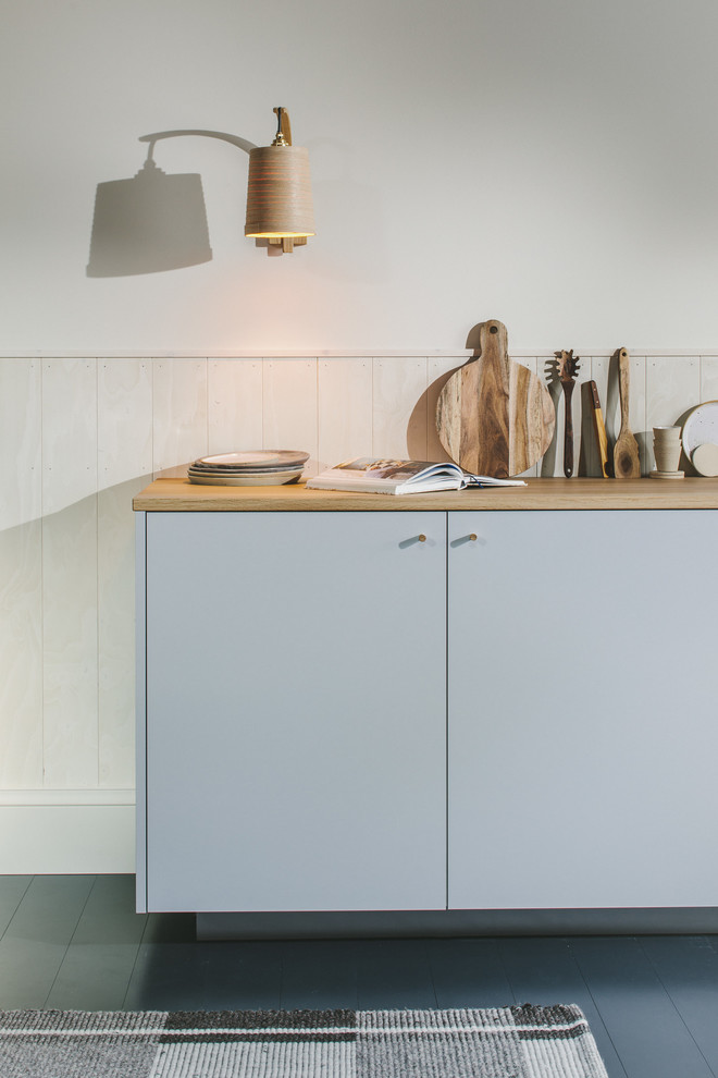 Inspiration för små minimalistiska linjära brunt kök med öppen planlösning, med en enkel diskho, släta luckor, grå skåp, träbänkskiva, vitt stänkskydd, stänkskydd i trä, integrerade vitvaror, målat trägolv och svart golv