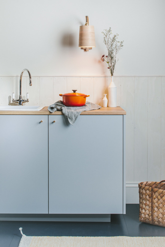 Foto på ett litet minimalistiskt brun linjärt kök med öppen planlösning, med en enkel diskho, släta luckor, grå skåp, träbänkskiva, vitt stänkskydd, stänkskydd i trä, integrerade vitvaror, målat trägolv och svart golv