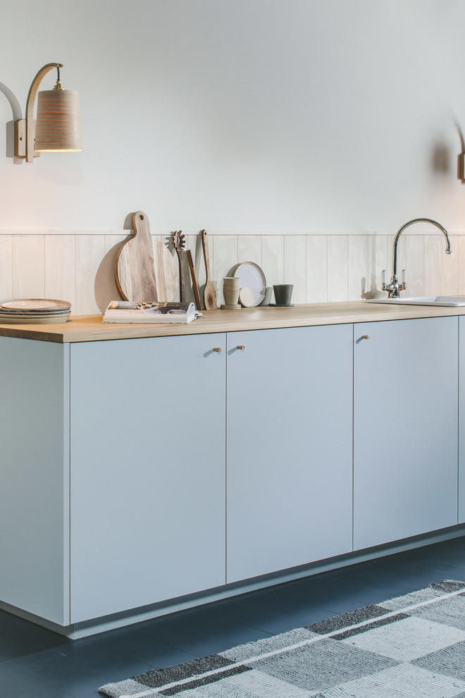 Bild på ett litet skandinaviskt brun linjärt brunt kök med öppen planlösning, med en enkel diskho, släta luckor, grå skåp, träbänkskiva, vitt stänkskydd, stänkskydd i trä, integrerade vitvaror, målat trägolv och svart golv