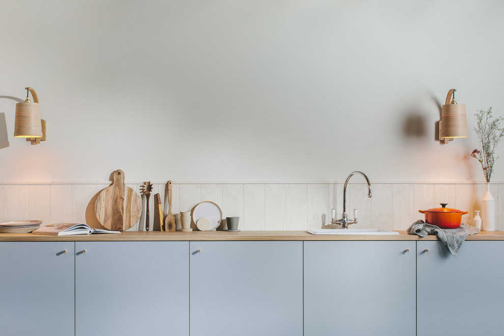 Idéer för små minimalistiska linjära brunt kök med öppen planlösning, med en enkel diskho, släta luckor, grå skåp, träbänkskiva, vitt stänkskydd, stänkskydd i trä, integrerade vitvaror, målat trägolv och svart golv