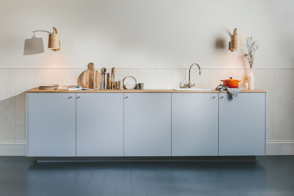 Photo of a small scandinavian single-wall open plan kitchen in Other with a single-bowl sink, flat-panel cabinets, grey cabinets, wood worktops, white splashback, wood splashback, integrated appliances, painted wood flooring, no island, black floors and brown worktops.