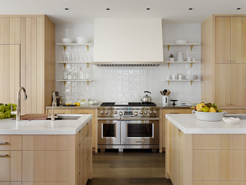 Diseño de cocina campestre con fregadero bajoencimera, armarios con paneles lisos, puertas de armario de madera clara, salpicadero blanco, electrodomésticos de acero inoxidable, suelo de madera oscura, dos o más islas, suelo marrón y encimeras blancas