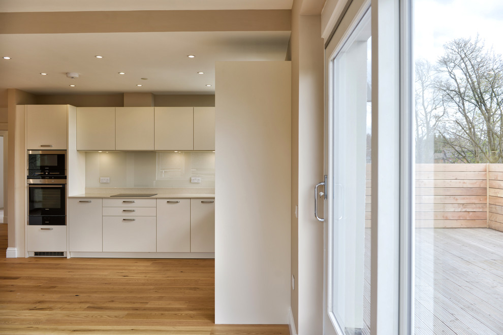 Ispirazione per una cucina contemporanea di medie dimensioni con lavello a doppia vasca, ante lisce, ante bianche, top in superficie solida, paraspruzzi beige, paraspruzzi con lastra di vetro, elettrodomestici da incasso, pavimento in legno massello medio e nessuna isola