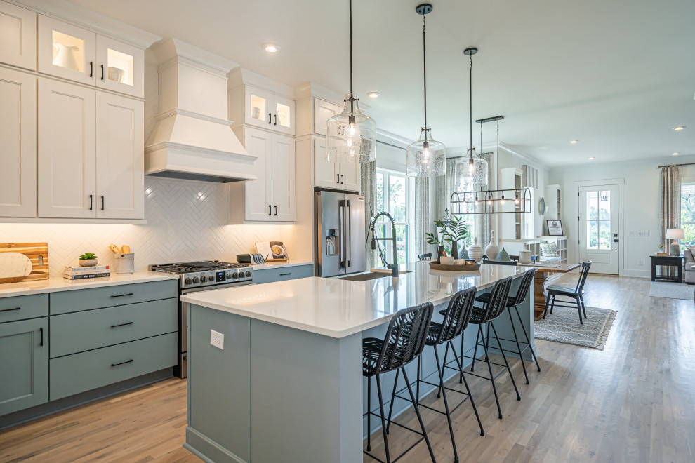 This is an example of a farmhouse galley kitchen in Other with a belfast sink, recessed-panel cabinets, blue cabinets, white splashback, stainless steel appliances, medium hardwood flooring, an island, brown floors and white worktops.