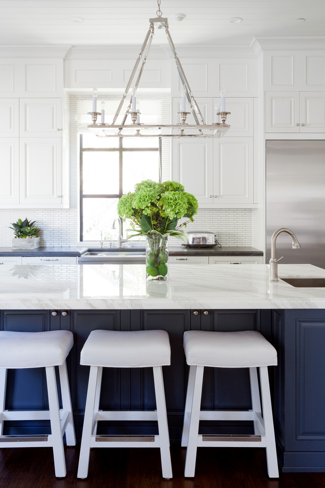 Geräumige Klassische Küche mit weißen Schränken, Küchenrückwand in Weiß, Kücheninsel, Waschbecken, profilierten Schrankfronten, Küchengeräten aus Edelstahl und braunem Holzboden in Los Angeles