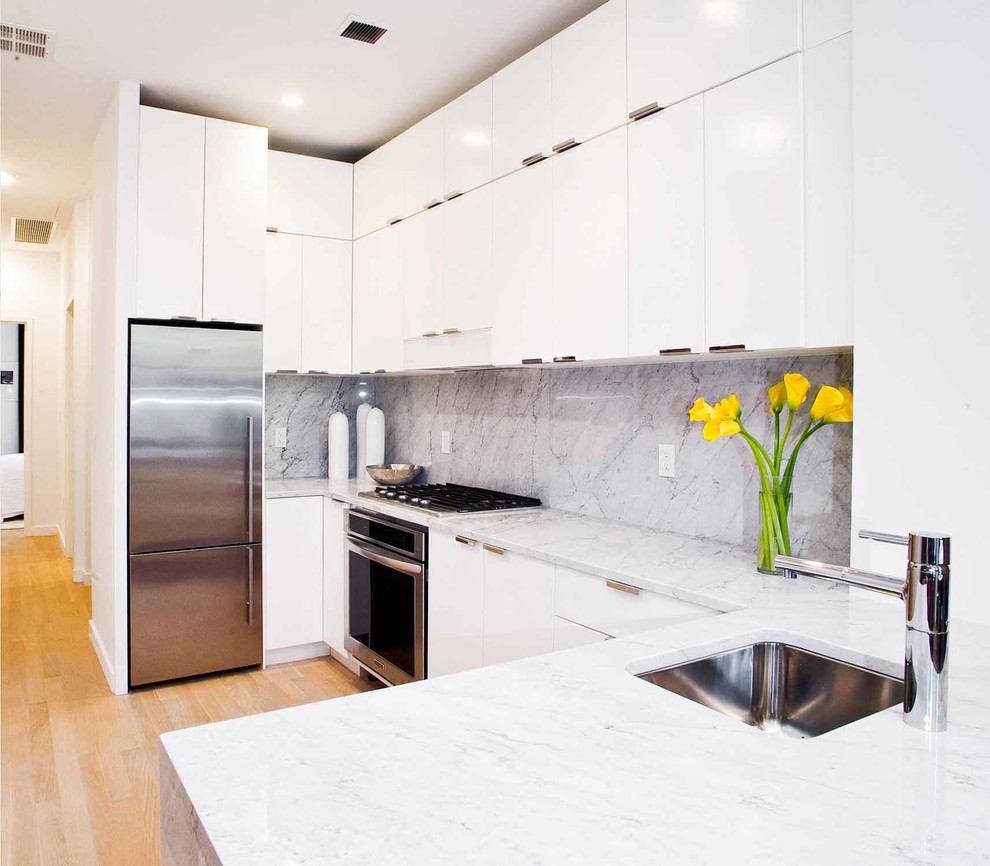 Open concept kitchen - mid-sized modern u-shaped light wood floor and beige floor open concept kitchen idea in New York with an undermount sink, flat-panel cabinets, white cabinets, marble countertops, gray backsplash, marble backsplash, stainless steel appliances and a peninsula
