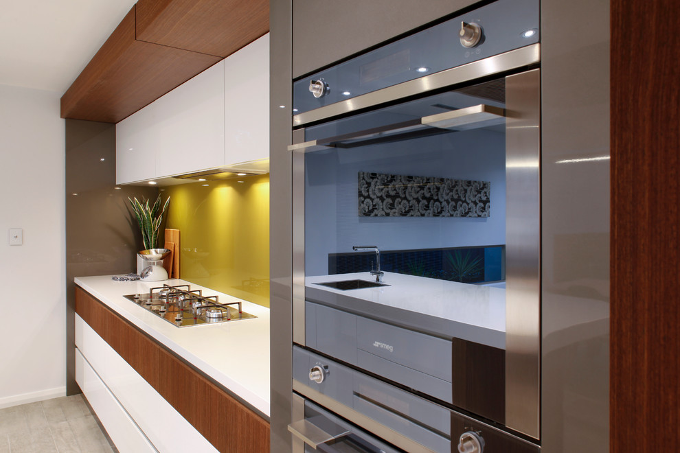 This is an example of a large contemporary galley kitchen pantry in Perth with an integrated sink, white cabinets, engineered stone countertops, green splashback, glass sheet splashback, stainless steel appliances and an island.