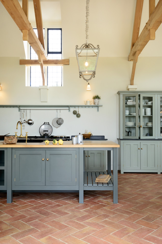 Large farmhouse single-wall open plan kitchen in Other with a belfast sink, beaded cabinets, grey cabinets, granite worktops, black appliances, terracotta flooring and an island.