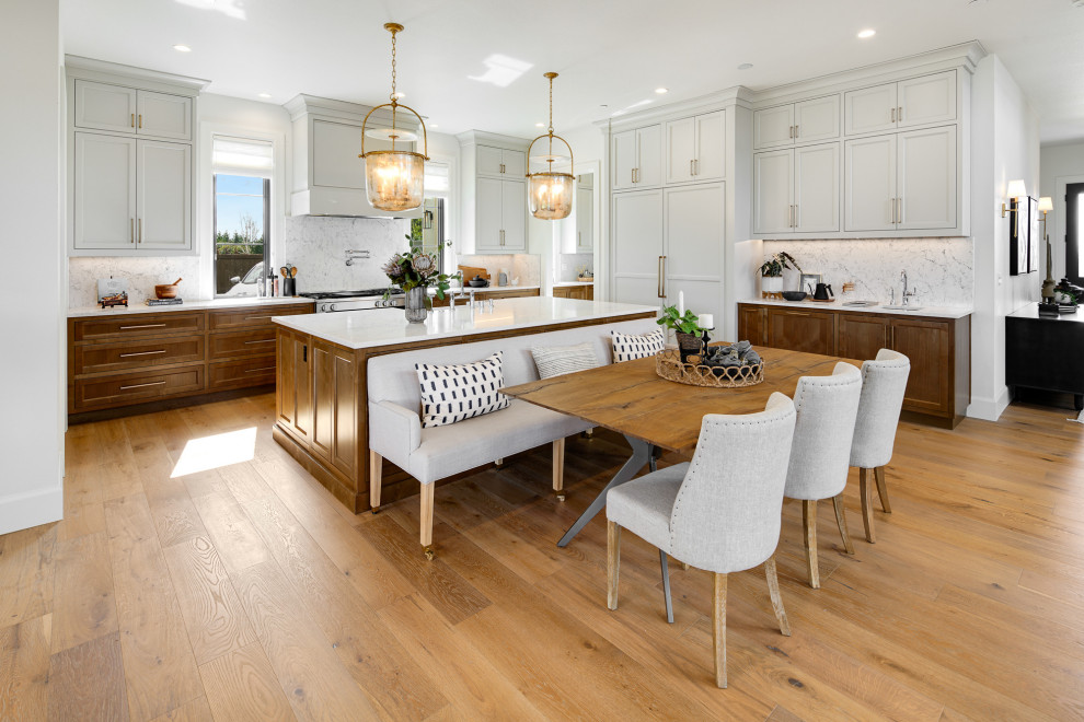 Modelo de cocinas en L clásica renovada, abierta, con fregadero sobremueble, armarios estilo shaker, puertas de armario grises, salpicadero blanco, salpicadero de losas de piedra, electrodomésticos con paneles, suelo de madera en tonos medios, una isla, suelo marrón y encimeras blancas