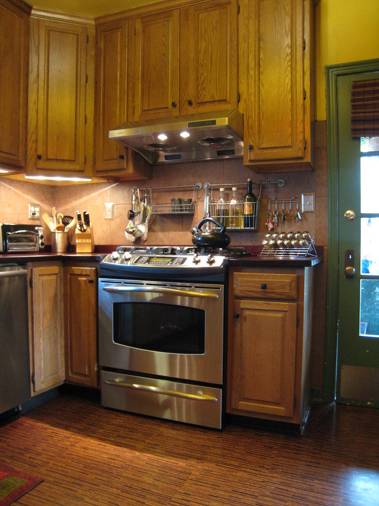 Bild på ett mellanstort amerikanskt u-kök, med stänkskydd i keramik, rostfria vitvaror, korkgolv, rött stänkskydd, luckor med upphöjd panel, skåp i mellenmörkt trä och kaklad bänkskiva