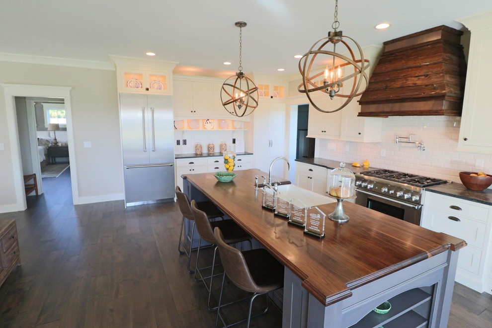 Foto på ett mellanstort lantligt kök, med en rustik diskho, luckor med profilerade fronter, vita skåp, träbänkskiva, vitt stänkskydd, stänkskydd i tunnelbanekakel, rostfria vitvaror, mörkt trägolv och en köksö