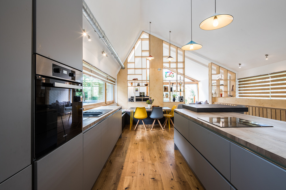 Design ideas for a large contemporary galley kitchen/diner in Other with a double-bowl sink, grey cabinets, wood worktops, window splashback, medium hardwood flooring, an island, brown floors, brown worktops, a vaulted ceiling and feature lighting.