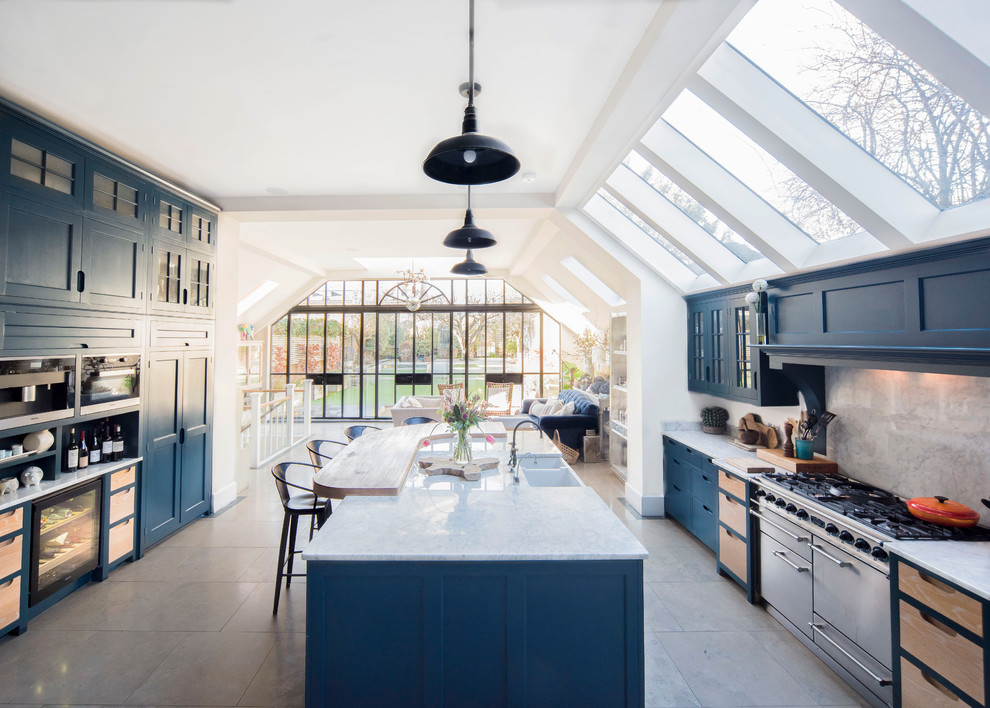 Photo of a traditional open plan kitchen in London with a belfast sink, blue cabinets, beige splashback, stone slab splashback, stainless steel appliances, an island, grey floors and white worktops.