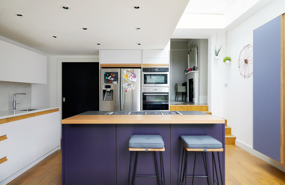 Moderne Wohnküche mit Quarzit-Arbeitsplatte, Küchenrückwand in Weiß, Küchengeräten aus Edelstahl, Kücheninsel, flächenbündigen Schrankfronten, weißen Schränken, braunem Holzboden und braunem Boden in London