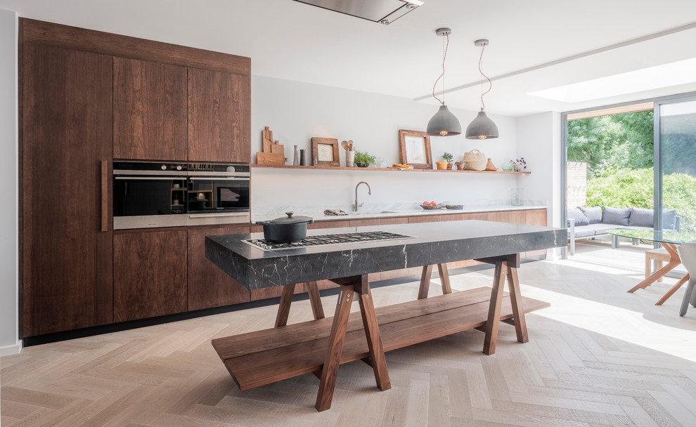 This is an example of a large contemporary single-wall open plan kitchen in London with an integrated sink, flat-panel cabinets, dark wood cabinets, marble worktops, stainless steel appliances, medium hardwood flooring, an island and white worktops.