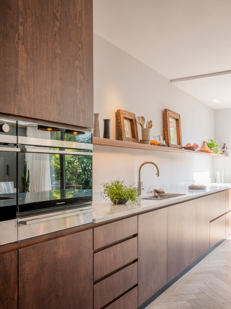Large contemporary single-wall open plan kitchen in London with an integrated sink, flat-panel cabinets, dark wood cabinets, marble worktops, stainless steel appliances, medium hardwood flooring, an island and white worktops.