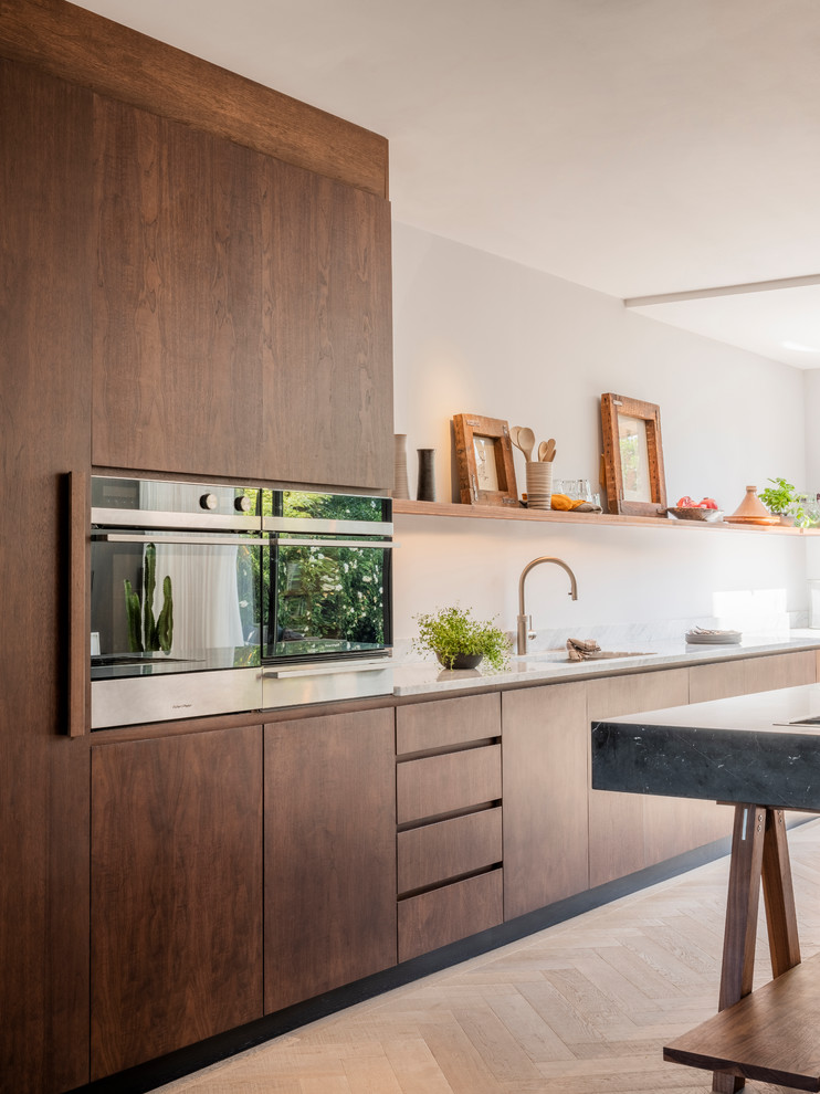 Inspiration for a large contemporary single-wall open plan kitchen in London with an integrated sink, flat-panel cabinets, dark wood cabinets, marble worktops, stainless steel appliances, medium hardwood flooring, an island and white worktops.