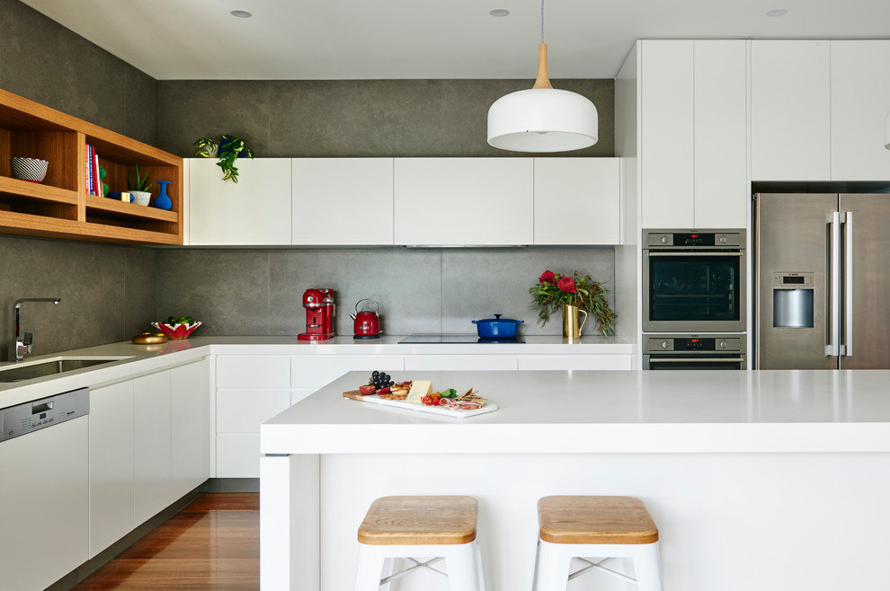 Idéer för ett modernt kök, med en undermonterad diskho, släta luckor, vita skåp, grått stänkskydd, stänkskydd i cementkakel, rostfria vitvaror, mellanmörkt trägolv, en köksö och brunt golv