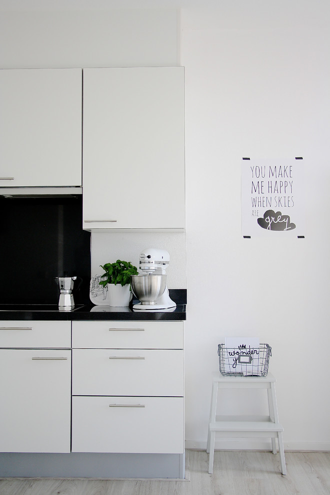 На фото: кухня в скандинавском стиле с плоскими фасадами, белыми фасадами и черным фартуком с