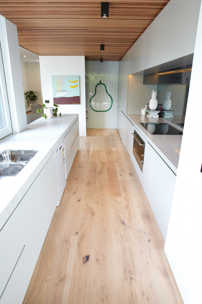 Foto di una cucina parallela scandinava di medie dimensioni con lavello sottopiano, ante lisce, ante bianche, top in granito, paraspruzzi nero, paraspruzzi con lastra di vetro, elettrodomestici bianchi e parquet chiaro