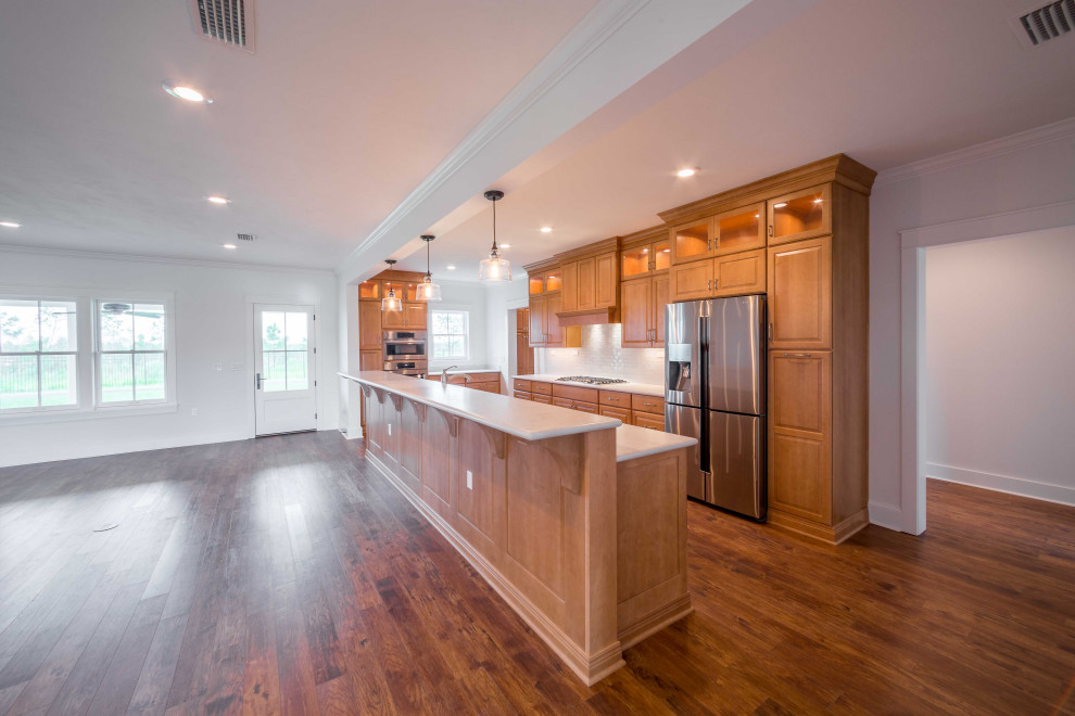 Example of a mid-sized classic galley medium tone wood floor and brown floor open concept kitchen design with an integrated sink, recessed-panel cabinets, medium tone wood cabinets, limestone countertops, white backsplash, mosaic tile backsplash, stainless steel appliances, an island and white countertops