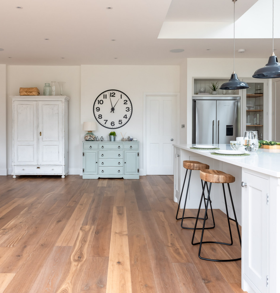 Design ideas for a large traditional u-shaped open plan kitchen in Surrey with shaker cabinets, white cabinets, quartz worktops, black appliances, light hardwood flooring, an island, brown floors and white worktops.