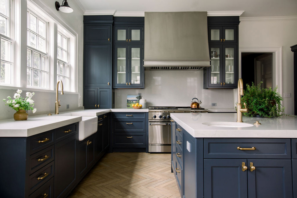 Traditional l-shaped kitchen in Chicago with a belfast sink, shaker cabinets, blue cabinets, white splashback, stainless steel appliances, light hardwood flooring, an island, beige floors and white worktops.