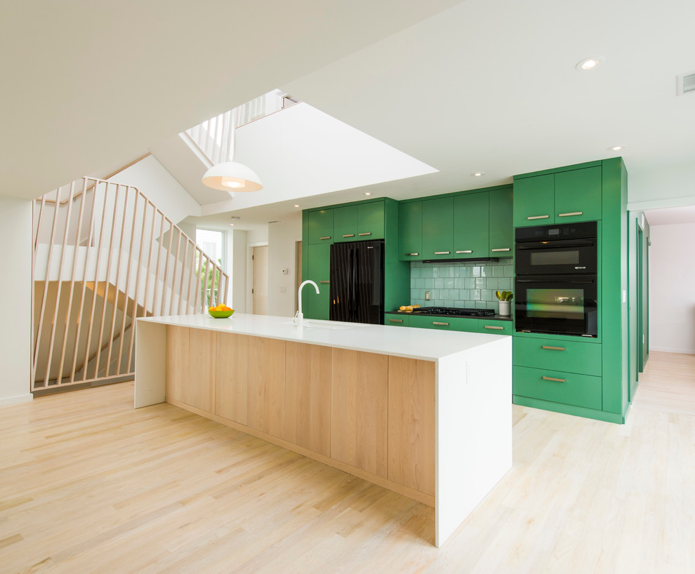 Example of a danish galley light wood floor open concept kitchen design in DC Metro with flat-panel cabinets, green cabinets, green backsplash, black appliances and an island