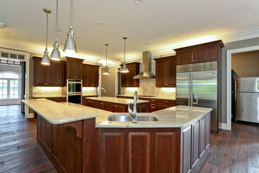 Example of a large classic l-shaped dark wood floor and brown floor eat-in kitchen design in Chicago with an undermount sink, raised-panel cabinets, dark wood cabinets, granite countertops, stainless steel appliances, two islands and white countertops