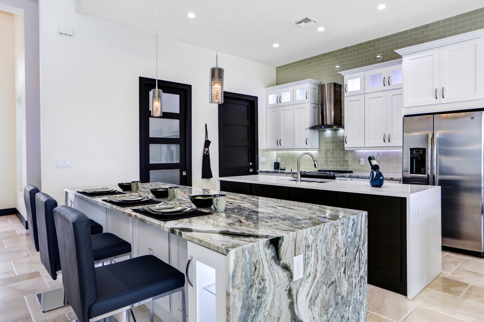 Large transitional travertine floor eat-in kitchen photo in Miami with a farmhouse sink, shaker cabinets, white cabinets, granite countertops, gray backsplash, subway tile backsplash, stainless steel appliances and two islands
