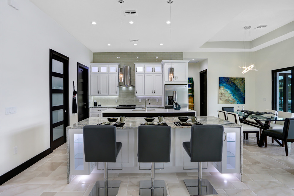 Large classic kitchen/diner in Miami with shaker cabinets, white cabinets, granite worktops, grey splashback, metro tiled splashback, stainless steel appliances, travertine flooring, multiple islands and a submerged sink.