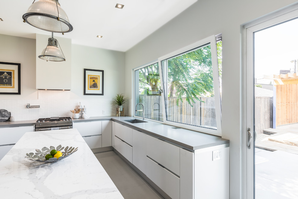 Large modern u-shaped enclosed kitchen in Toronto with a submerged sink, flat-panel cabinets, white cabinets, engineered stone countertops, white splashback, matchstick tiled splashback, stainless steel appliances, concrete flooring, an island, grey floors and white worktops.