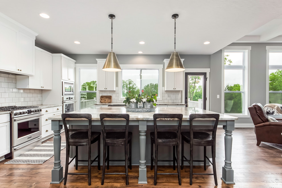 Beach style medium tone wood floor open concept kitchen photo in Columbus with shaker cabinets, white cabinets, white backsplash, subway tile backsplash, stainless steel appliances, an island and gray countertops