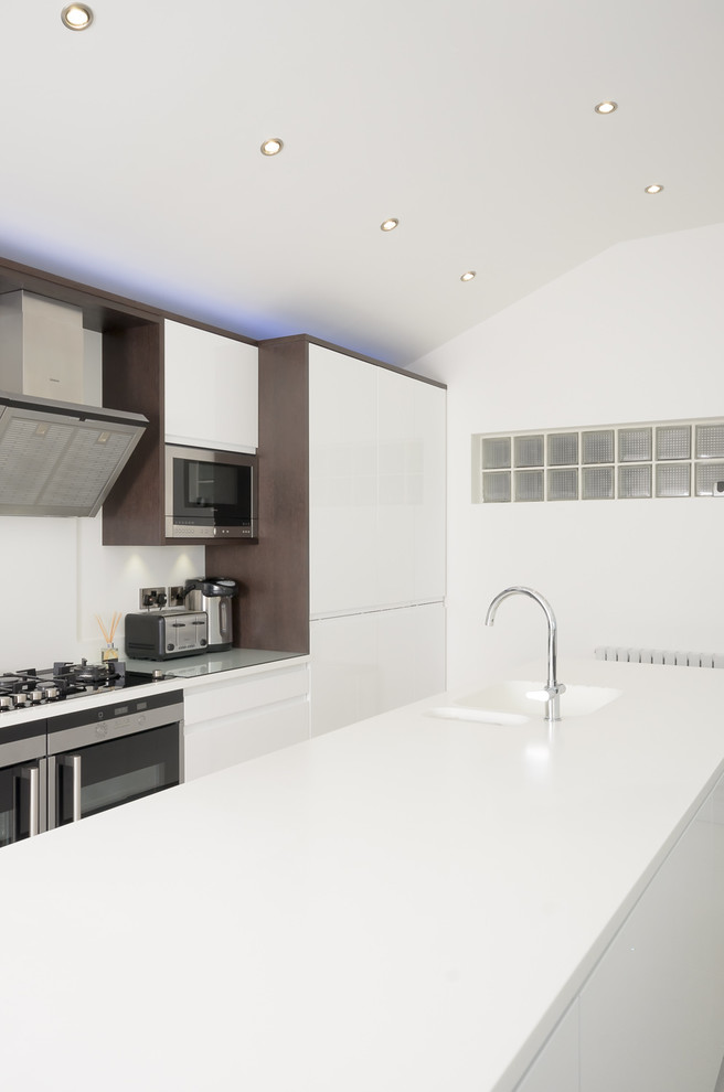 Große Moderne Küche mit integriertem Waschbecken, weißen Schränken, Mineralwerkstoff-Arbeitsplatte, Küchenrückwand in Weiß und Elektrogeräten mit Frontblende in Sonstige