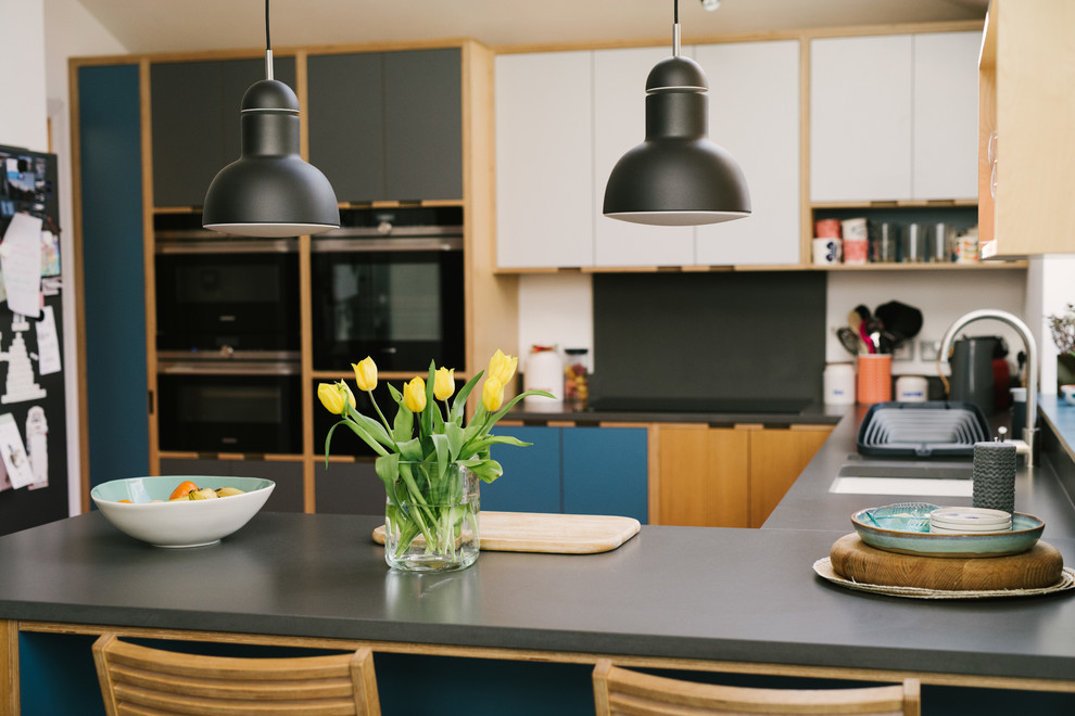Foto di una cucina contemporanea di medie dimensioni con lavello sottopiano, ante lisce, ante blu, paraspruzzi grigio, elettrodomestici neri, penisola, pavimento arancione e top grigio