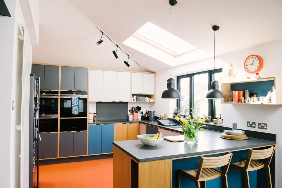 Réalisation d'une cuisine design de taille moyenne avec un évier encastré, un placard à porte plane, des portes de placard bleues, une crédence grise, un électroménager noir, une péninsule, un sol orange et un plan de travail gris.