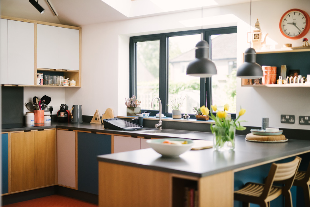 Cette image montre une cuisine design de taille moyenne avec un évier encastré, un placard à porte plane, des portes de placard bleues, une crédence grise, un électroménager noir, une péninsule, un sol orange et un plan de travail gris.