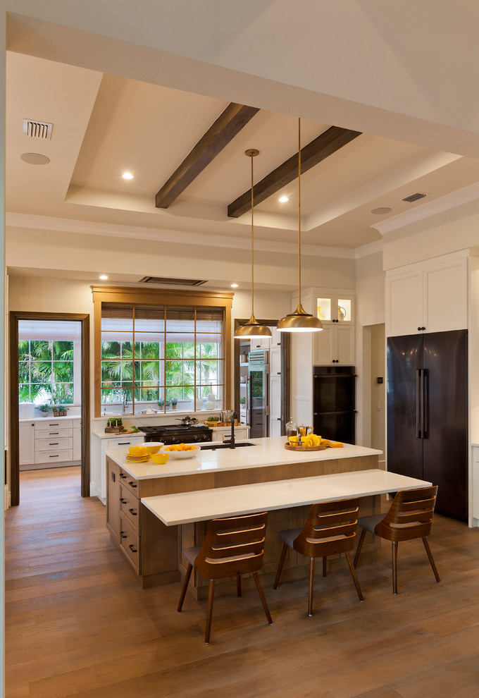 Photo of a large classic u-shaped enclosed kitchen in Tampa with a submerged sink, shaker cabinets, white cabinets, composite countertops, yellow splashback, metro tiled splashback, stainless steel appliances, medium hardwood flooring, an island, brown floors and white worktops.