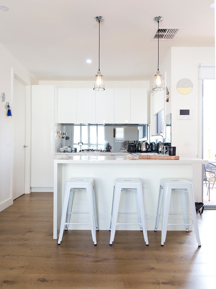 Moderne Küche in U-Form mit flächenbündigen Schrankfronten, weißen Schränken, Rückwand aus Spiegelfliesen, dunklem Holzboden, Halbinsel und braunem Boden in Melbourne