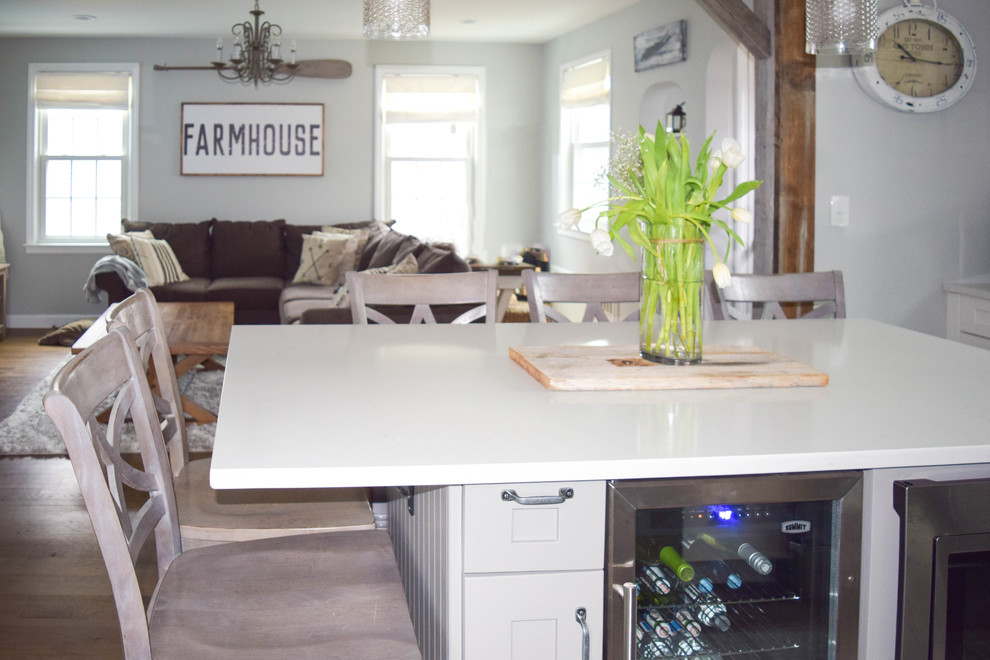 Example of a mid-sized cottage chic l-shaped dark wood floor eat-in kitchen design in New York with a farmhouse sink, shaker cabinets, gray cabinets, quartz countertops, gray backsplash, stone tile backsplash, stainless steel appliances and an island