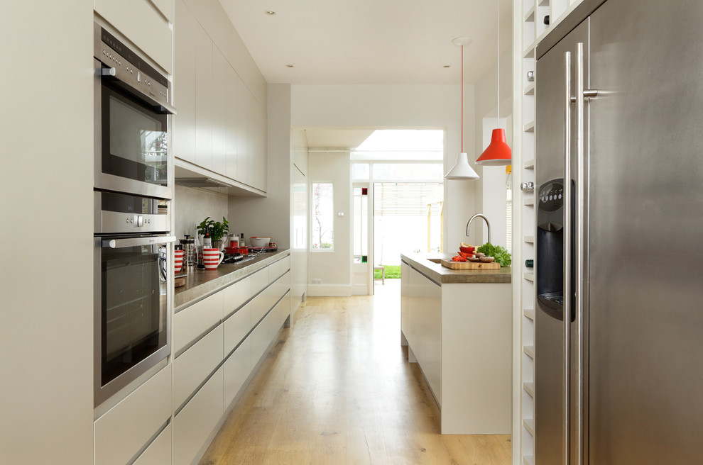 Contemporary kitchen/diner in London with flat-panel cabinets, white cabinets, concrete worktops, integrated appliances and an island.