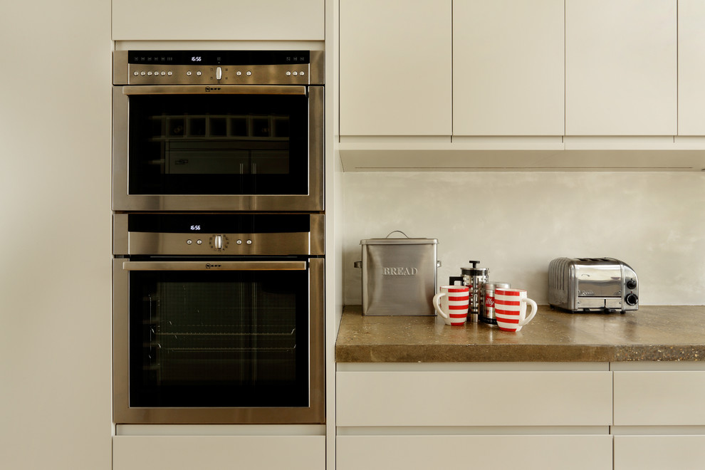 Ejemplo de cocina comedor actual con armarios con paneles lisos, puertas de armario blancas, encimera de cemento, electrodomésticos con paneles y una isla