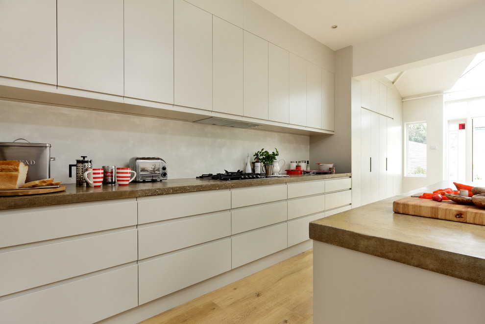 Diseño de cocina contemporánea con armarios con paneles lisos, puertas de armario blancas, encimera de cemento, electrodomésticos con paneles y una isla