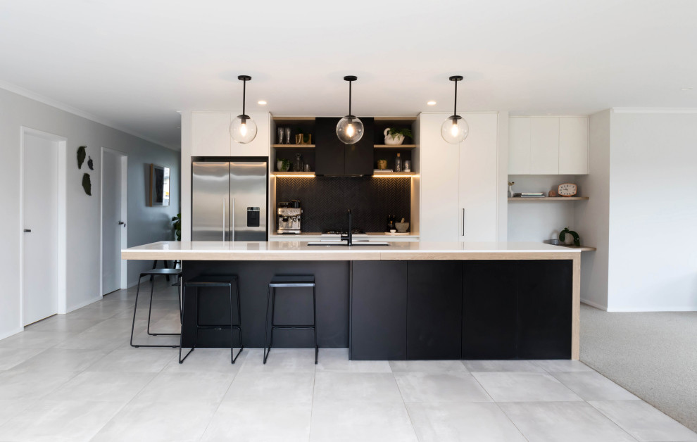 Example of a large trendy galley gray floor kitchen design in Auckland with an undermount sink, flat-panel cabinets, white cabinets, black backsplash, stainless steel appliances, an island and white countertops