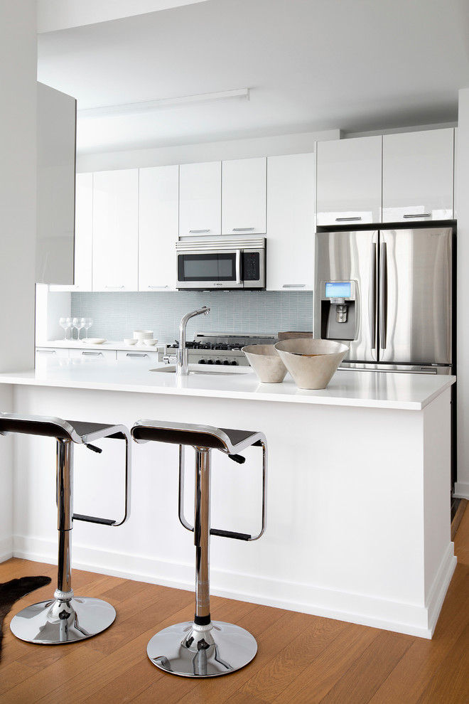 Mittelgroße Moderne Küche mit Unterbauwaschbecken, flächenbündigen Schrankfronten, weißen Schränken, Küchenrückwand in Blau, Küchengeräten aus Edelstahl, braunem Holzboden und Halbinsel in New York