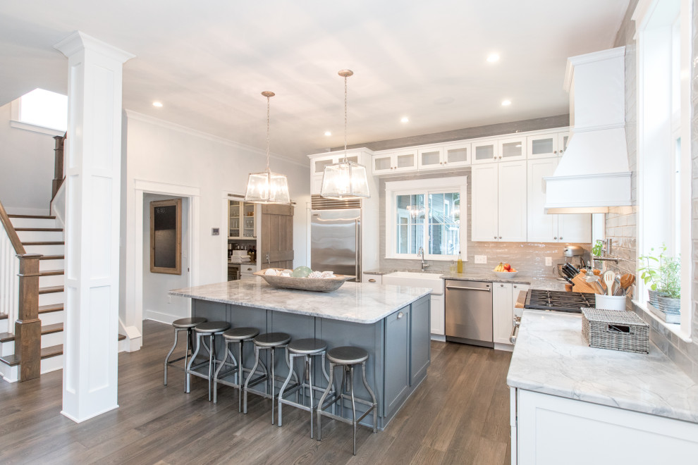 Inspiration for a coastal u-shaped medium tone wood floor and brown floor open concept kitchen remodel in Other with a farmhouse sink, shaker cabinets, white cabinets, marble countertops, beige backsplash, subway tile backsplash, stainless steel appliances, an island and gray countertops