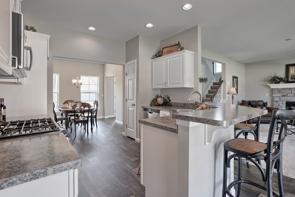 Photo of a medium sized rural u-shaped kitchen/diner in Other with a double-bowl sink, white cabinets, laminate countertops, stainless steel appliances, vinyl flooring and a breakfast bar.